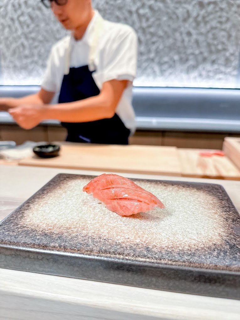 piece of sushi on table with chef in background